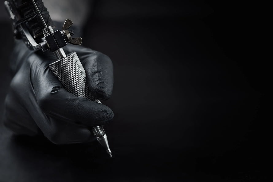 Close-up of a gloved hand holding a professional tattoo machine against a dark background HD wallpaper