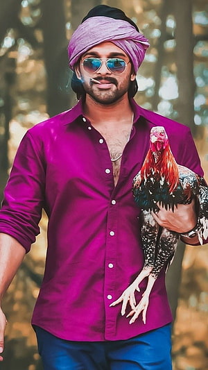 Allu Arjun as Pushpa in vibrant magenta shirt and turban holding a rooster in a forest setting HD phone wallpaper
