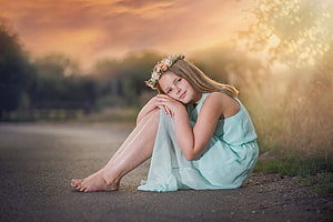 Young girl in mint dress with floral crown sitting barefoot on a road at golden hour HD wallpaper