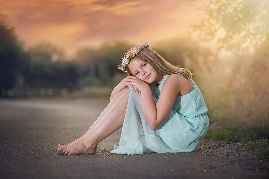 Young girl in mint dress with floral crown sitting barefoot on a road at golden hour HD wallpaper