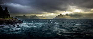 Dramatic Stormy Seascape with Distant Mountains and Rocky Coastline HD wallpaper