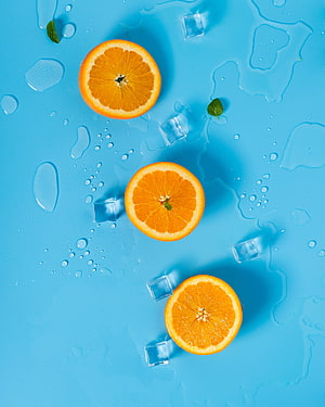 Fresh orange slices with ice cubes and mint leaves on a vibrant blue background HD phone wallpaper