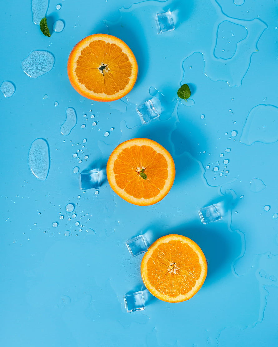 Fresh orange slices with ice cubes and mint leaves on a vibrant blue background HD phone wallpaper