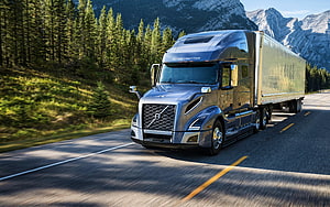 Volvo VNL 760 semi-truck hauling a cargo trailer on a scenic mountain highway HD wallpaper