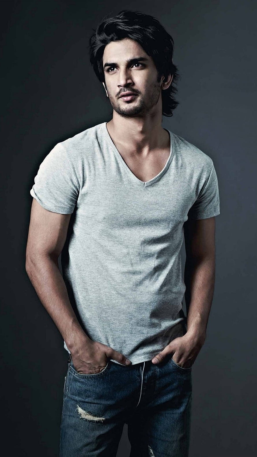 Sushant Singh Rajput in a grey v-neck t-shirt and distressed jeans against a dark studio backdrop HD phone wallpaper