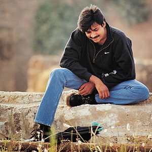Pawan Kalyan sitting on a stone ledge in a black Nike jacket and blue jeans HD phone wallpaper