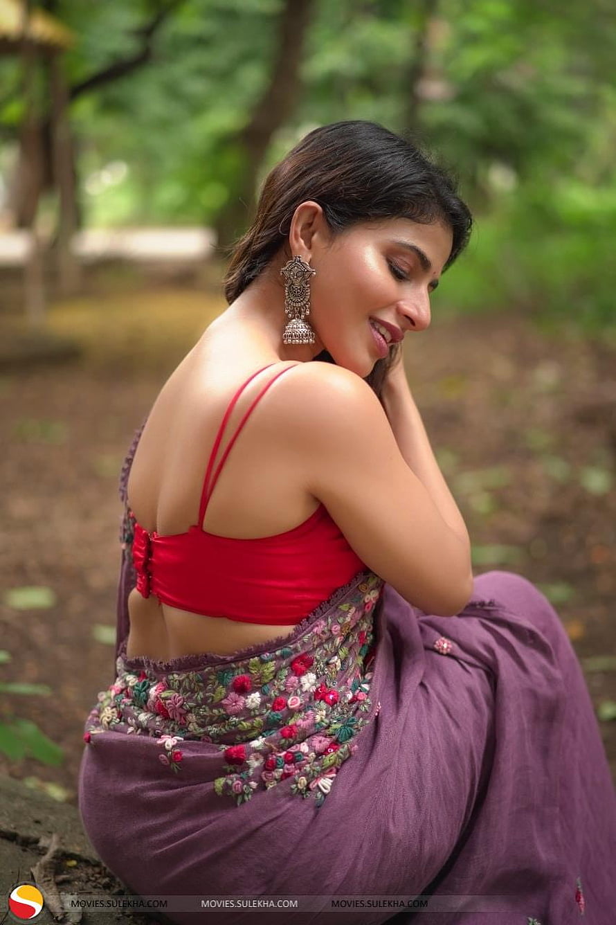 Iswarya Menon in a red blouse and embroidered purple saree seated in a lush green forest HD phone wallpaper