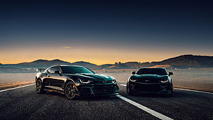 Two Black Chevrolet Camaro Muscle Cars Parked on a Desert Road at Sunset HD wallpaper