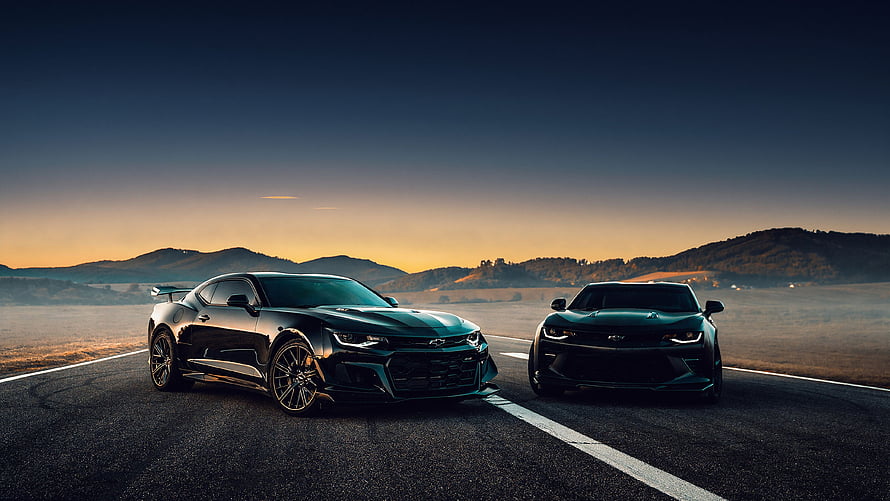 Two Black Chevrolet Camaro Muscle Cars Parked on a Desert Road at Sunset HD wallpaper