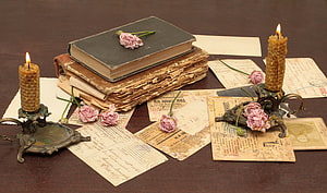 Vintage still life with old books, handwritten letters, beeswax candles, and pink roses on a dark wooden table HD wallpaper