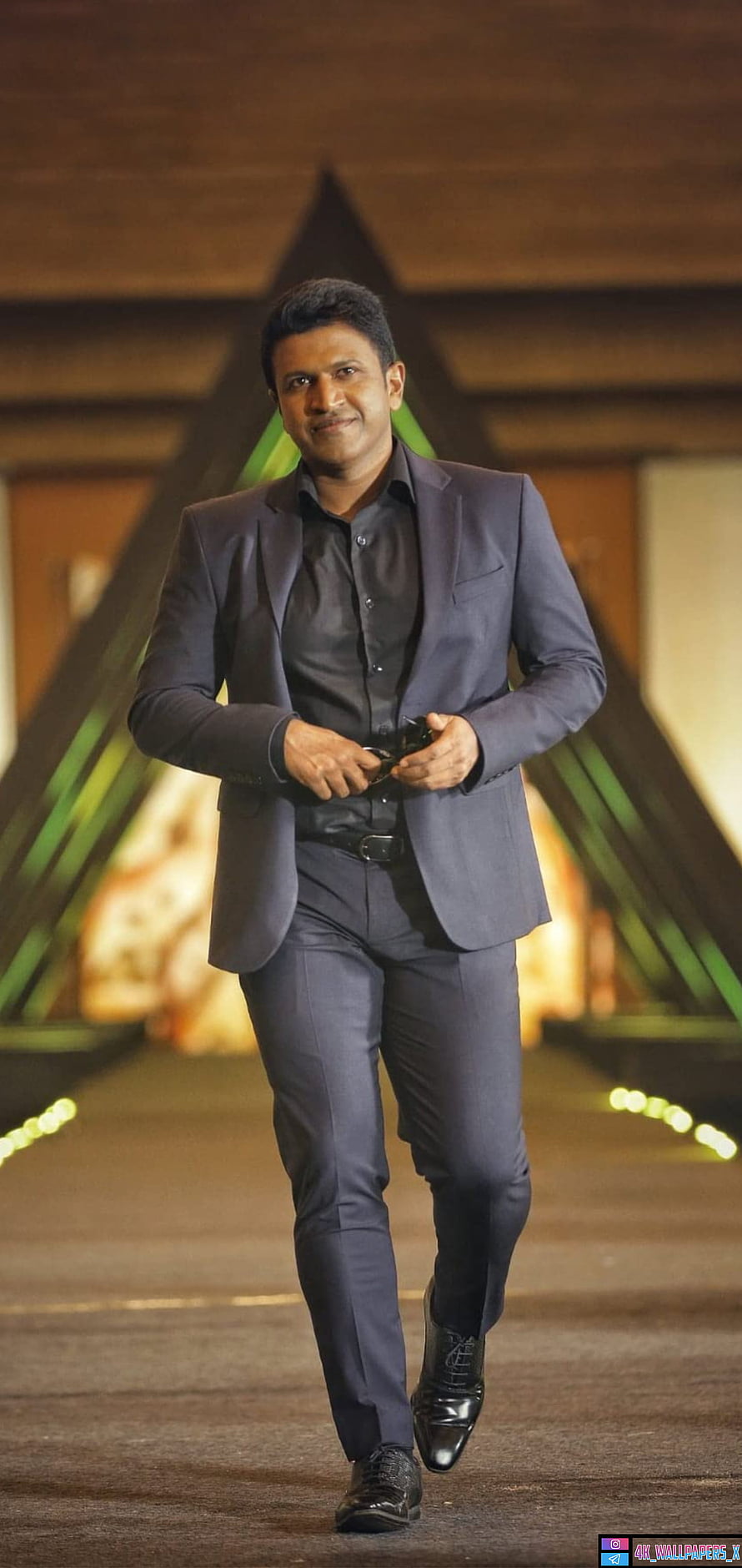 Puneeth Rajkumar in a stylish grey suit walking on a runway with dramatic lighting HD phone wallpaper