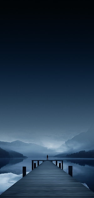 Solitary Figure on a Misty Lake Pier at Night with Distant Mountains HD phone wallpaper