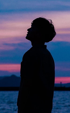 Silhouette of a Young Man Gazing at a Vibrant Twilight Sky Over Water HD phone wallpaper