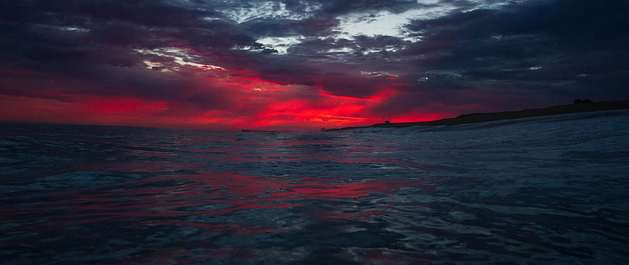 Dramatic Crimson Sunset Over Dark Ocean Waves with Moody Clouds HD wallpaper