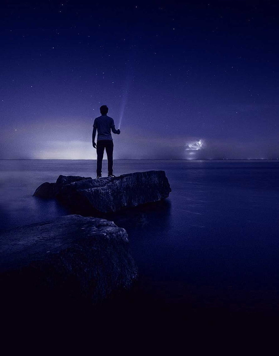 Silhouette of a person standing on a rock gazing at a starry night sky over calm water HD phone wallpaper