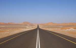 Endless Desert Highway Stretching Toward Distant Sand Dunes Under a Clear Blue Sky HD wallpaper