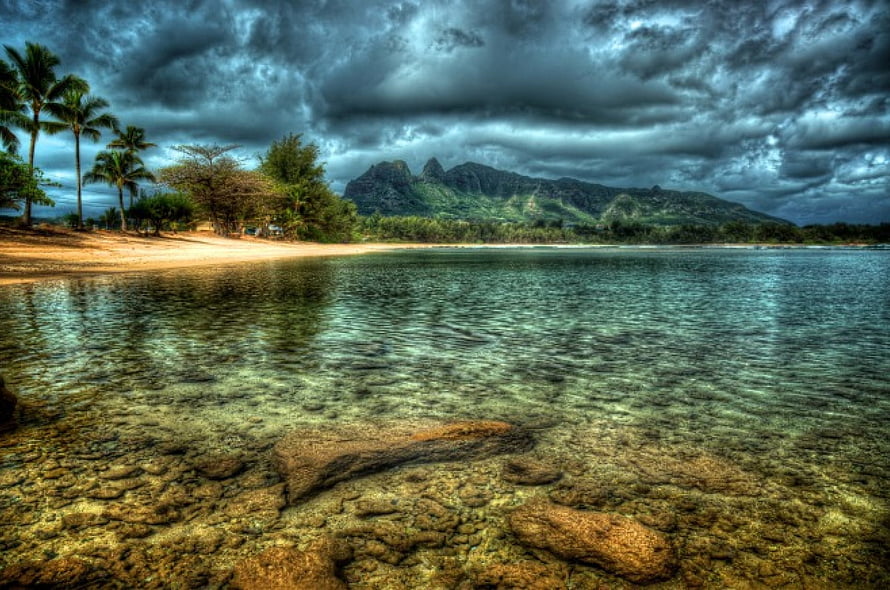Tropical Lagoon with Clear Shallow Water, Palm Trees, and Dramatic Stormy Sky Over Distant Mountains HD wallpaper