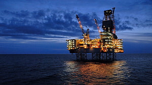 Illuminated Offshore Oil Rig Standing Alone in the Ocean at Dusk HD wallpaper