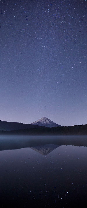 Snow-Capped Volcano Reflected in a Still Lake Beneath a Star-Filled Night Sky HD phone wallpaper