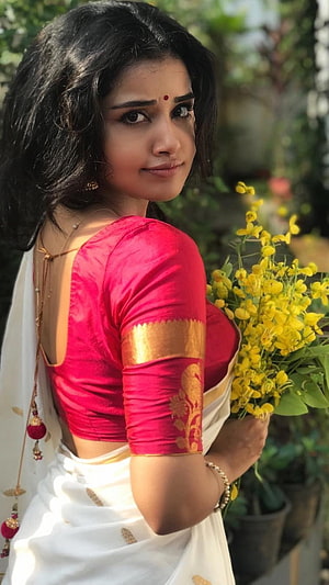 Anupama Parameswaran in a white saree with a pink blouse holding yellow flowers HD phone wallpaper