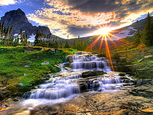 Sunrise over a cascading mountain waterfall with dramatic clouds and alpine peaks HD wallpaper