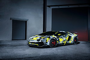 Lamborghini Aventador SV LP750-4 with bold yellow and grey camouflage livery in a dark industrial garage HD wallpaper