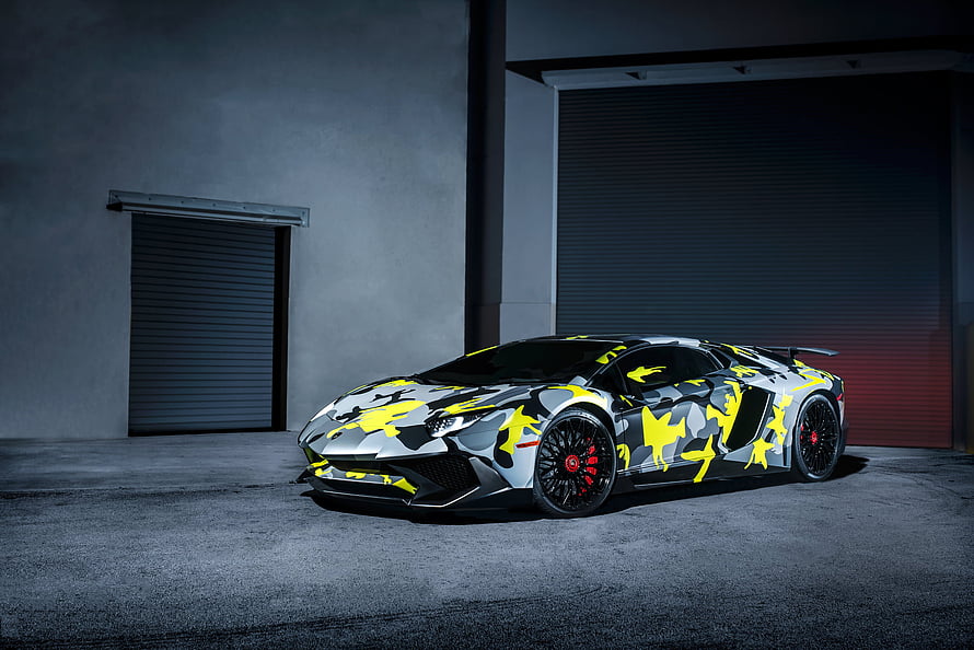 Lamborghini Aventador SV LP750-4 with bold yellow and grey camouflage livery in a dark industrial garage HD wallpaper