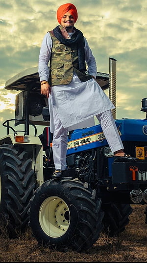 Sidhu Moose Wala standing on a blue New Holland tractor in a field HD phone wallpaper