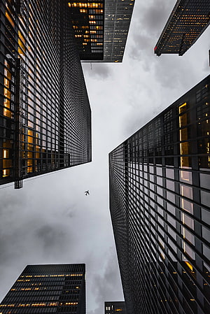 Dramatic Low-Angle View of Modern Skyscrapers and Airplane Against Overcast Sky HD phone wallpaper