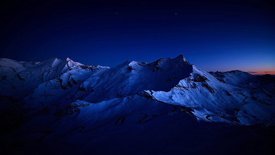 Snow-Capped Mountain Range at Night with Winding Road and Deep Blue Sky HD wallpaper