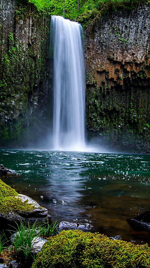 Towering Waterfall Plunging Into a Deep Green Pool Surrounded by Mossy Cliffs HD phone wallpaper