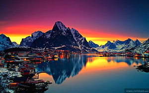 Vibrant Sunset Over Snow-Capped Mountains and Coastal Village with Calm Water Reflections HD wallpaper