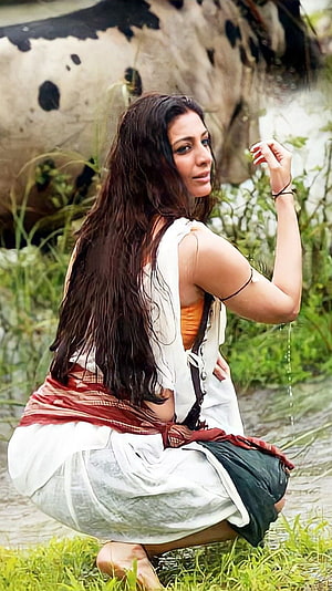 Tabu in Traditional Attire Crouching by a River with a Cow in the Background HD phone wallpaper