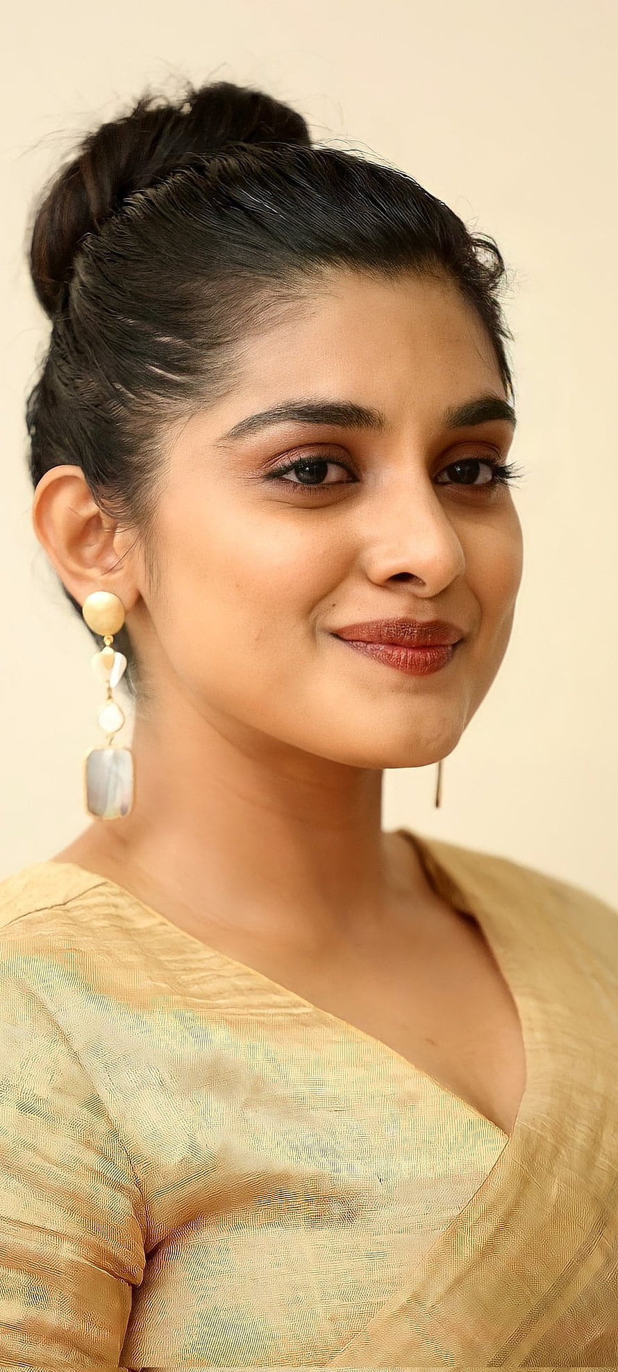 Nivetha Thomas in a golden saree with elegant dangling earrings and a neat bun hairstyle HD phone wallpaper
