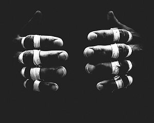 Black and white photograph of two hands with fingers wrapped in white tape against a dark background HD wallpaper