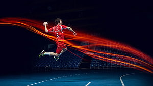 Handball Player in Red Kit Leaping with Ball in Dark Arena HD wallpaper