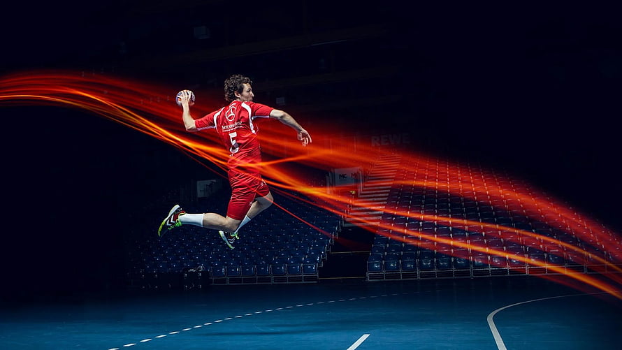 Handball Player in Red Kit Leaping with Ball in Dark Arena HD wallpaper