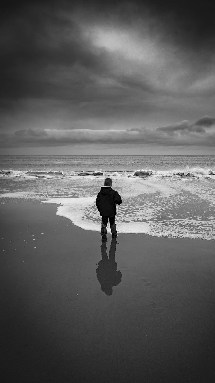 Solitary Boy Standing on Wet Sand Facing the Ocean Under a Stormy Sky HD phone wallpaper