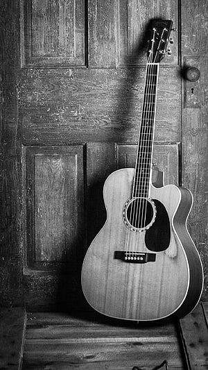 Vintage acoustic guitar leaning against a weathered wooden door in black and white HD phone wallpaper