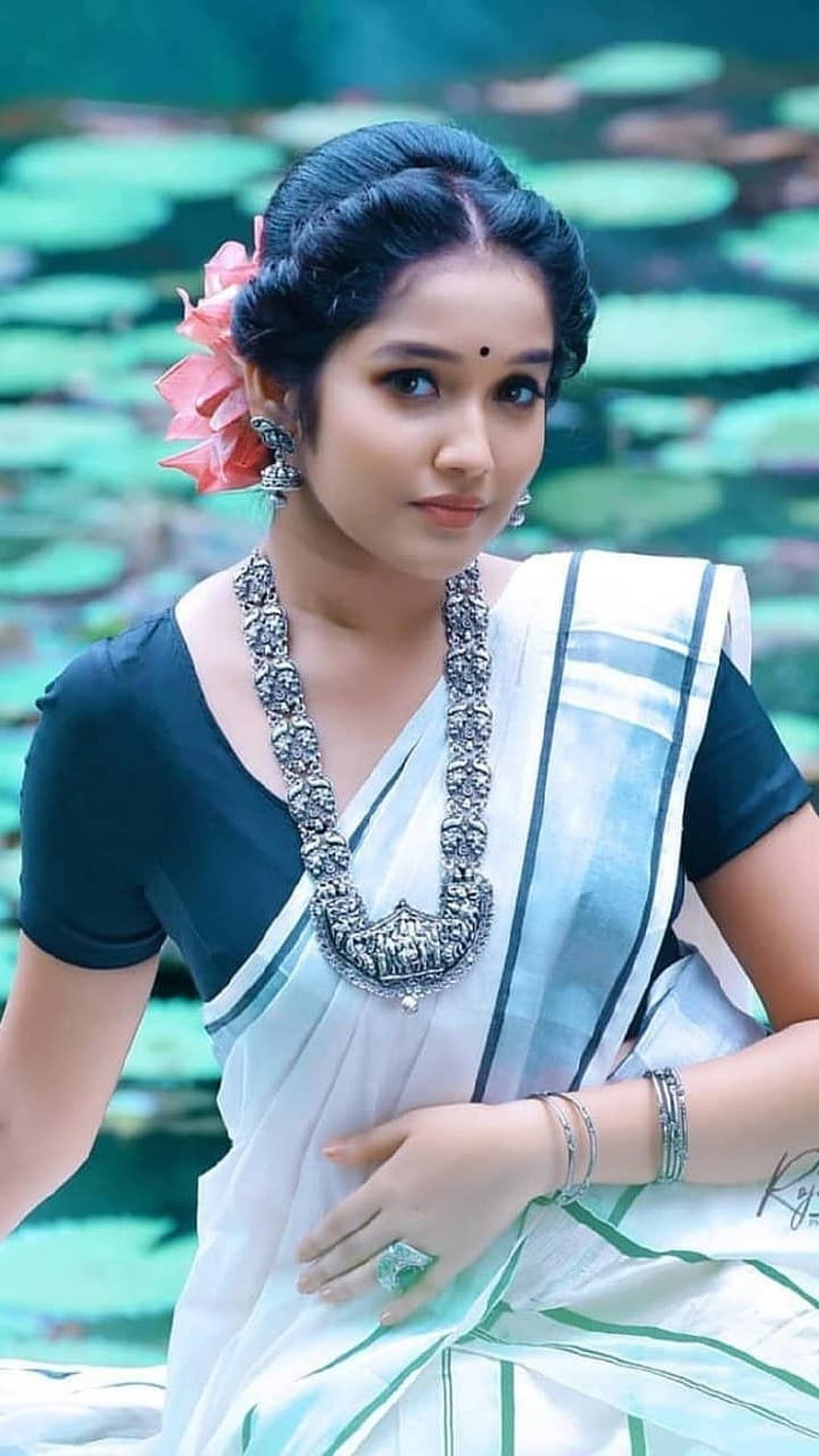Anikha Surendran in White Saree with Traditional Silver Jewelry and Lotus Pond Background HD phone wallpaper