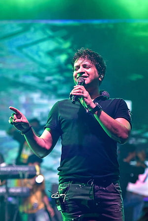 Singer KK performing live on stage with microphone under green concert lighting HD phone wallpaper