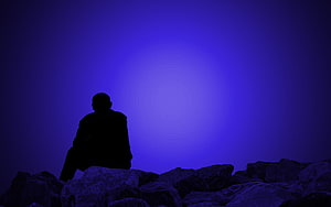 Silhouette of a Person Sitting on Rocks Against a Deep Blue Gradient Sky HD wallpaper