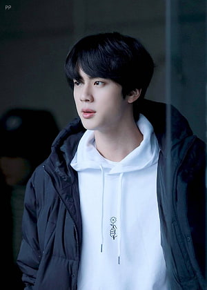 Jin BTS in a white hoodie and black jacket with a soft, contemplative expression HD phone wallpaper