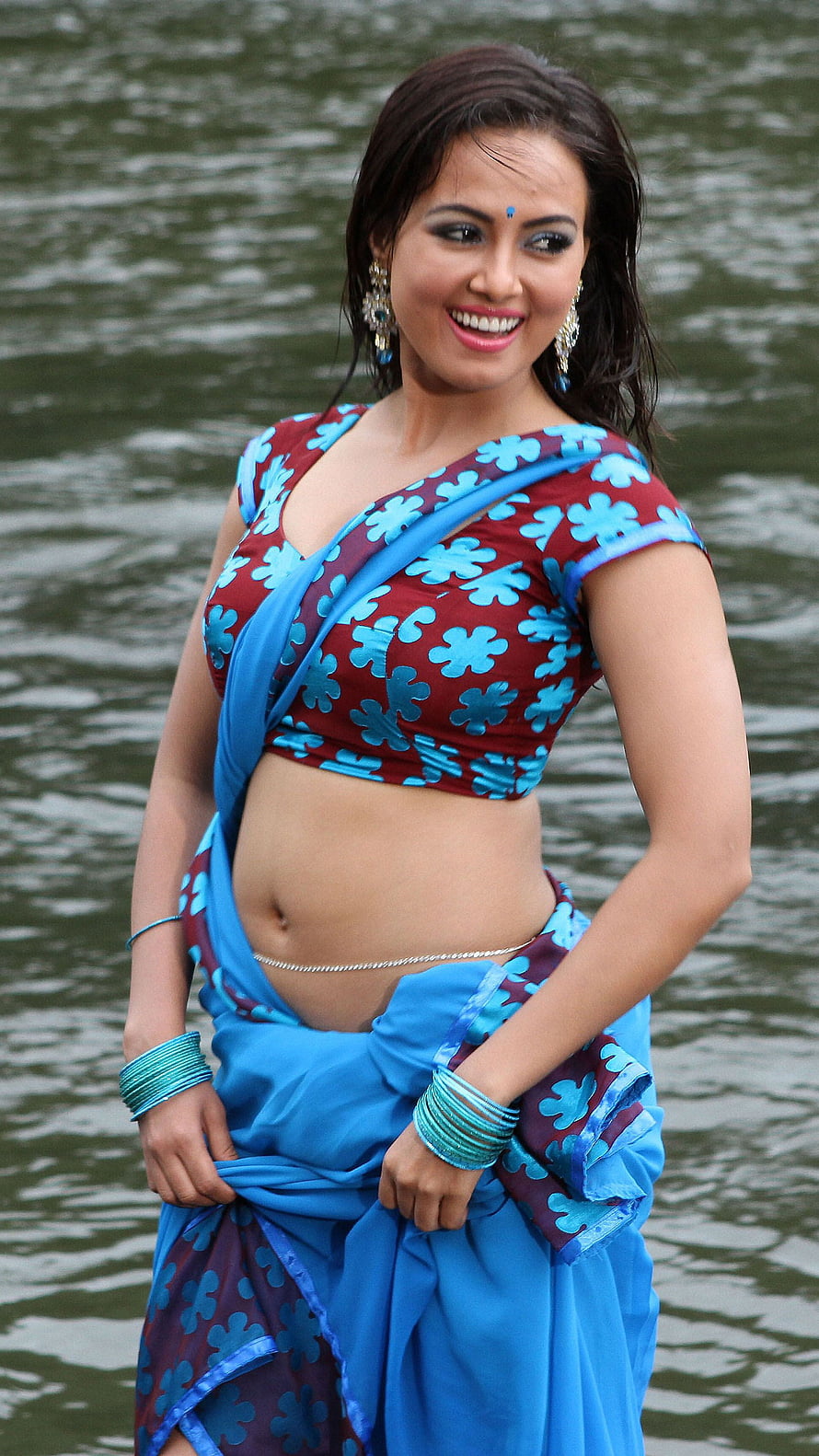 Sana Khan in a vibrant blue and maroon floral saree standing by a calm lake HD phone wallpaper