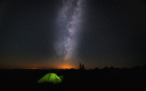 Glowing Green Tent Under the Milky Way Galaxy in a Dark Mountain Landscape HD wallpaper