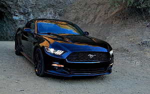 Black Ford Mustang GT parked on a dusty trail with a rocky cliff backdrop HD wallpaper