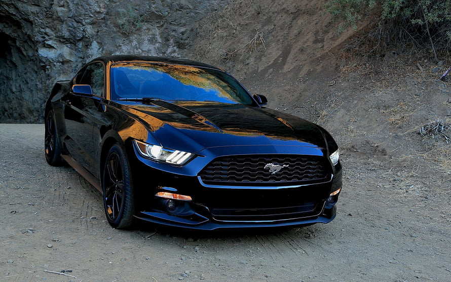 Black Ford Mustang GT parked on a dusty trail with a rocky cliff backdrop HD wallpaper
