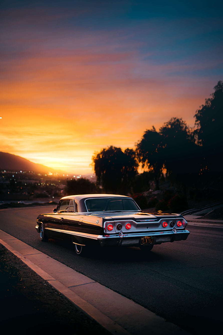 Classic 1960s American Sedan Parked on a Hillside Road at Golden Hour Sunset HD phone wallpaper