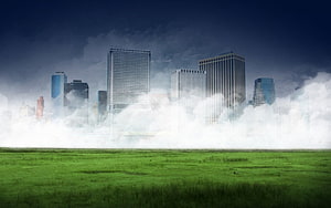 City skyline emerging from low fog over a vibrant green meadow under a dark stormy sky HD wallpaper