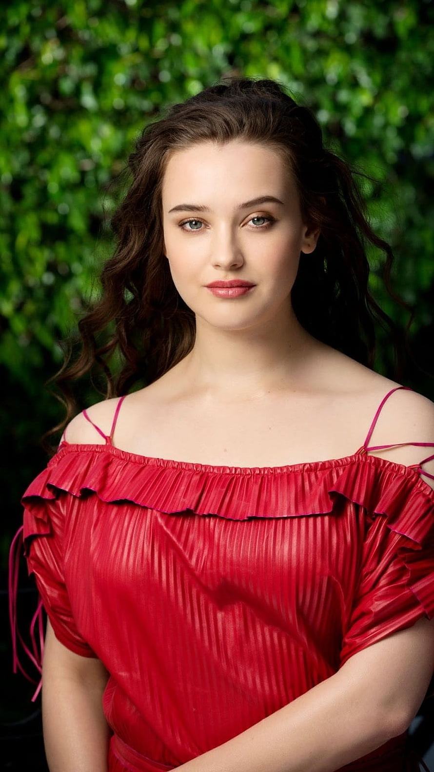 Katherine Langford in a red off-shoulder ruffled top against a green leafy background HD phone wallpaper